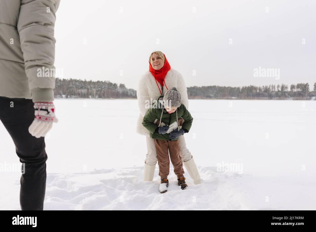 Femme souriante embrassant son fils regardant un homme debout sur la neige Banque D'Images