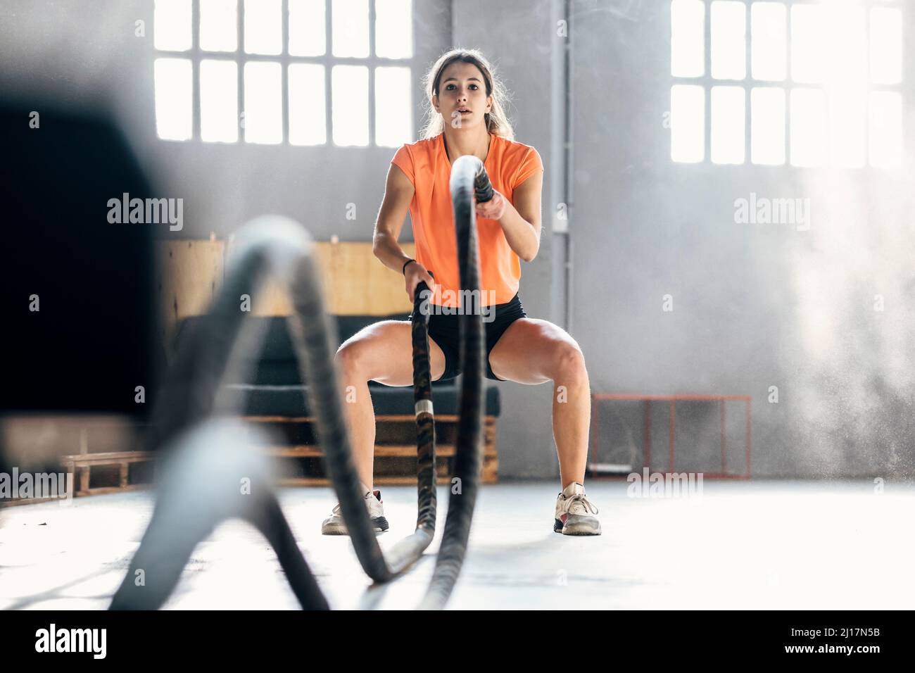 Jeune femme s'exerçant avec des cordes de combat dans la salle de gym Banque D'Images