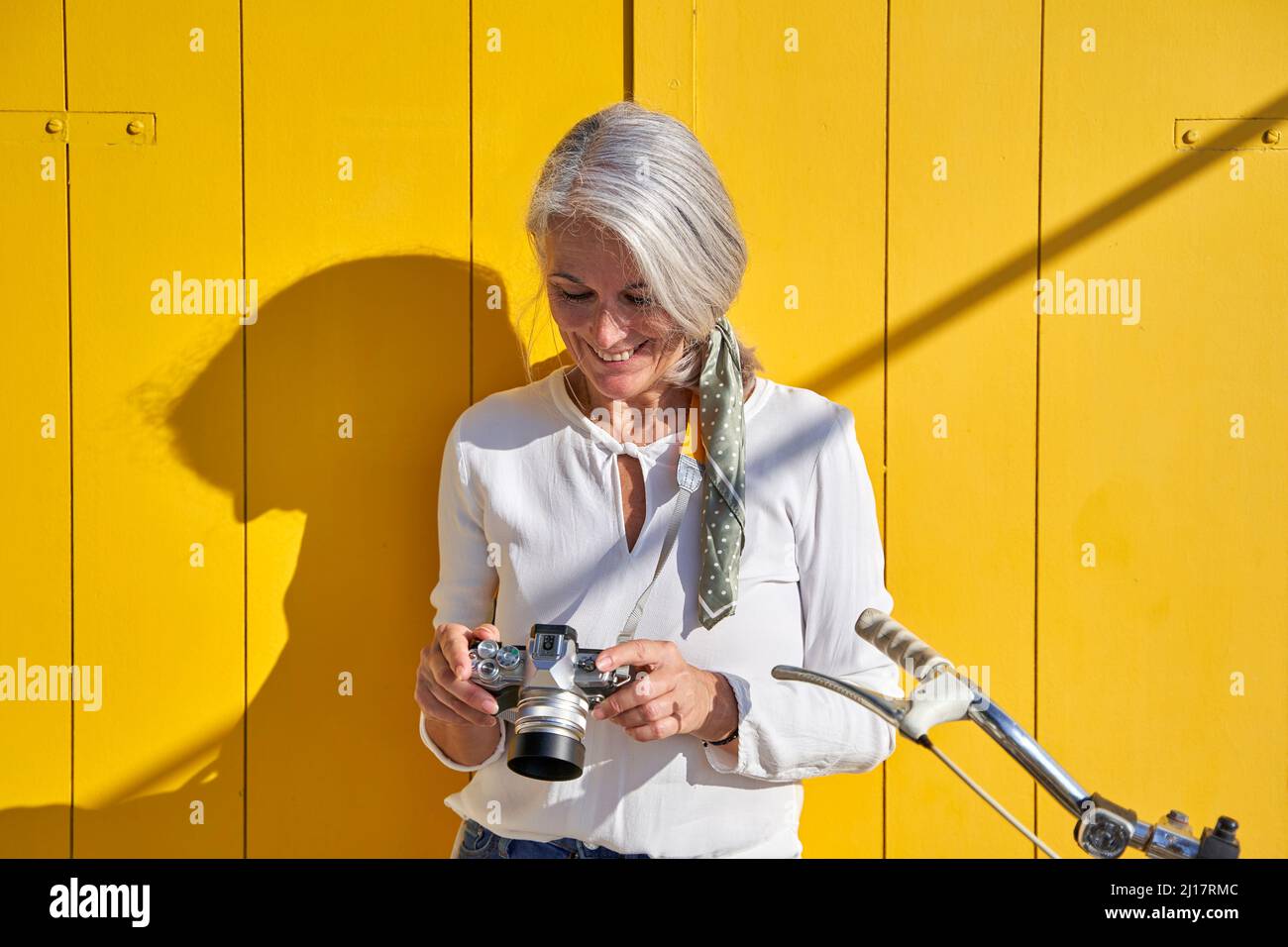 Femme souriante avec caméra debout devant la porte jaune par beau temps Banque D'Images