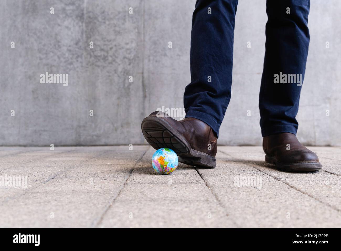 Homme mettant le pied sur le globe-jouet devant le mur Banque D'Images