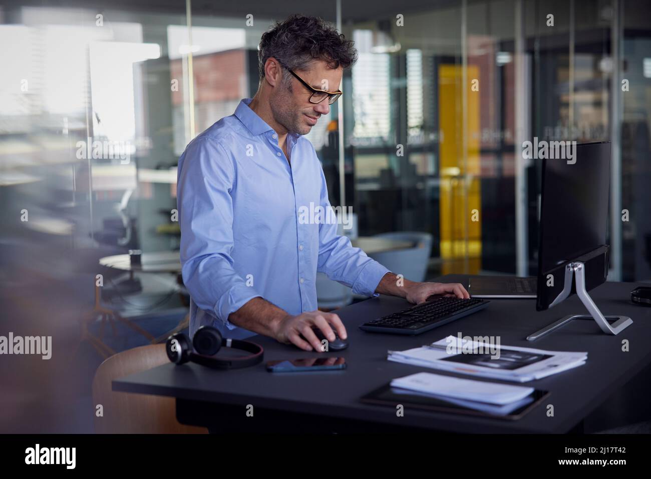 Homme d'affaires souriant portant des lunettes à l'aide d'un ordinateur se tenant au bureau Banque D'Images
