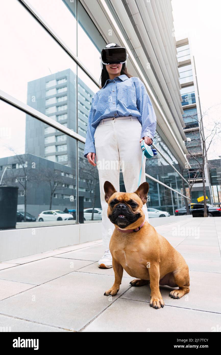 Bonne femme d'affaires portant un simulateur de réalité virtuelle debout avec un chien sur la piste Banque D'Images