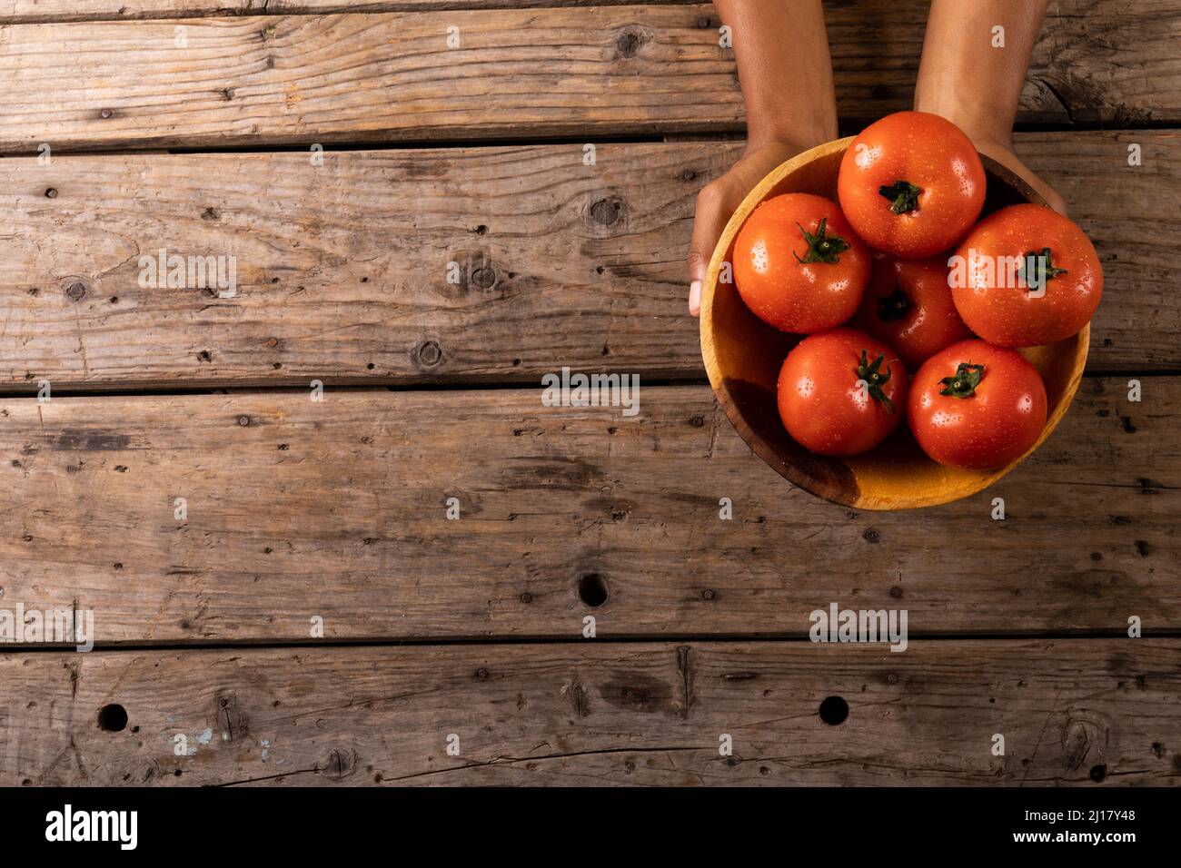 Directement au-dessus de la vue des mains cultivées tenant des tomates fraîches dans un bol sur une table en bois Banque D'Images