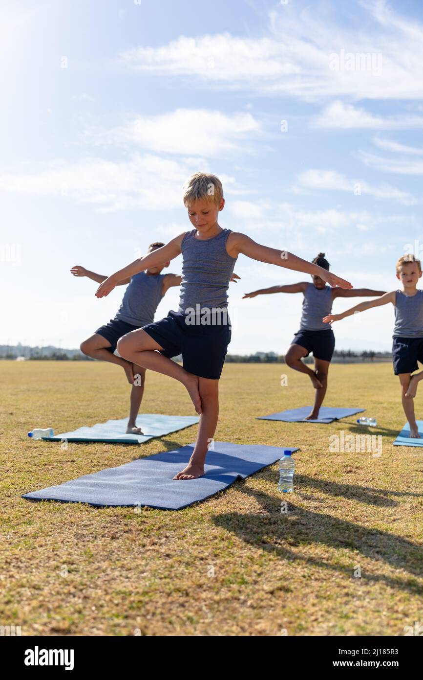 Garçons d'école élémentaire multiraciaux avec bras tendus debout sur une jambe pendant l'exercice Banque D'Images