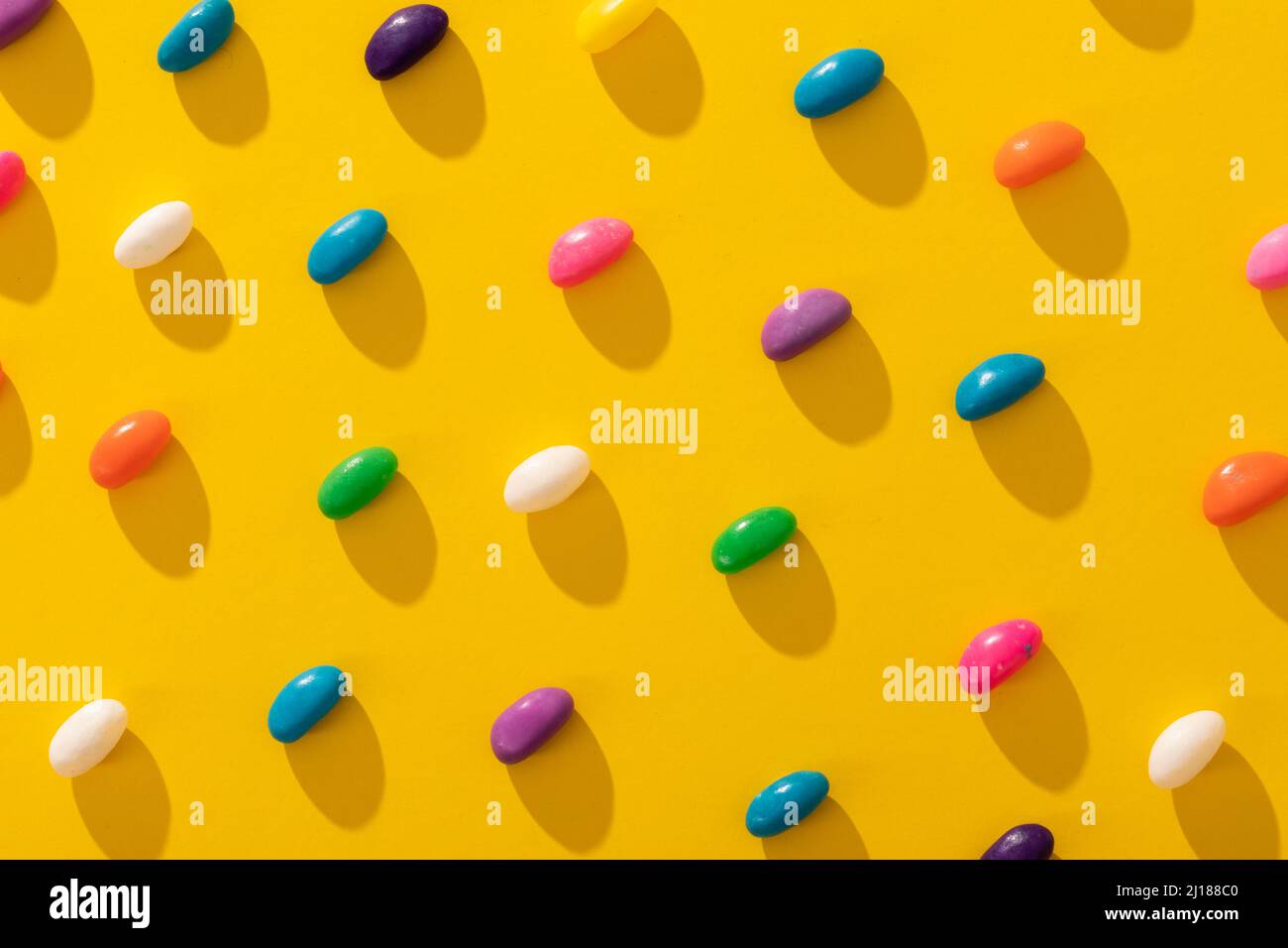 Photo plein format de bonbons multicolores disposés en rangée sur fond jaune Banque D'Images