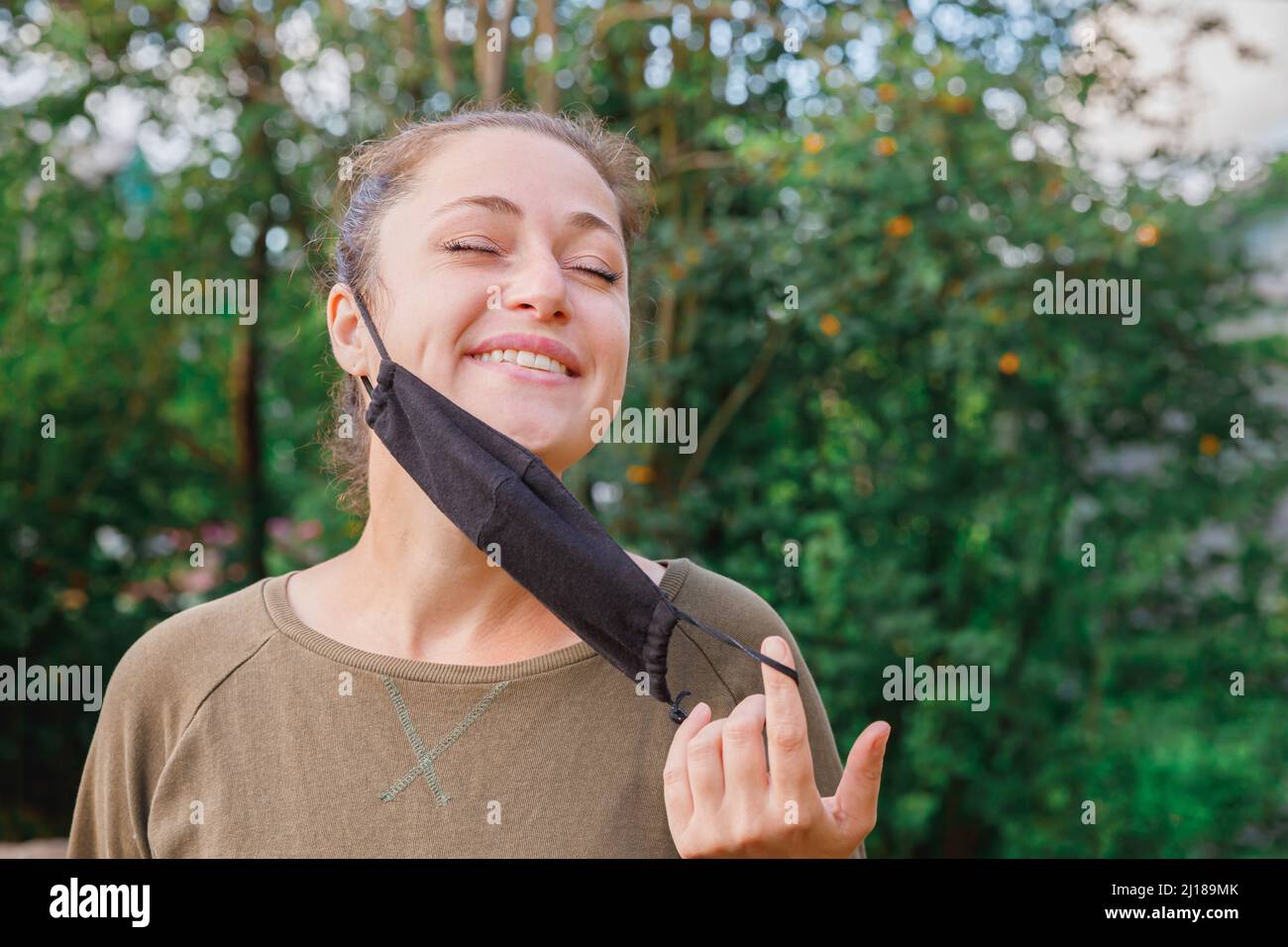 Bonne fille positive prend le masque médical de protection du visage à l'extérieur.Jeune femme qui retire le masque souriant après la vaccination.Pandémie de coronavirus Covid 19 concept.Fleurs de printemps allergie au pollen Banque D'Images