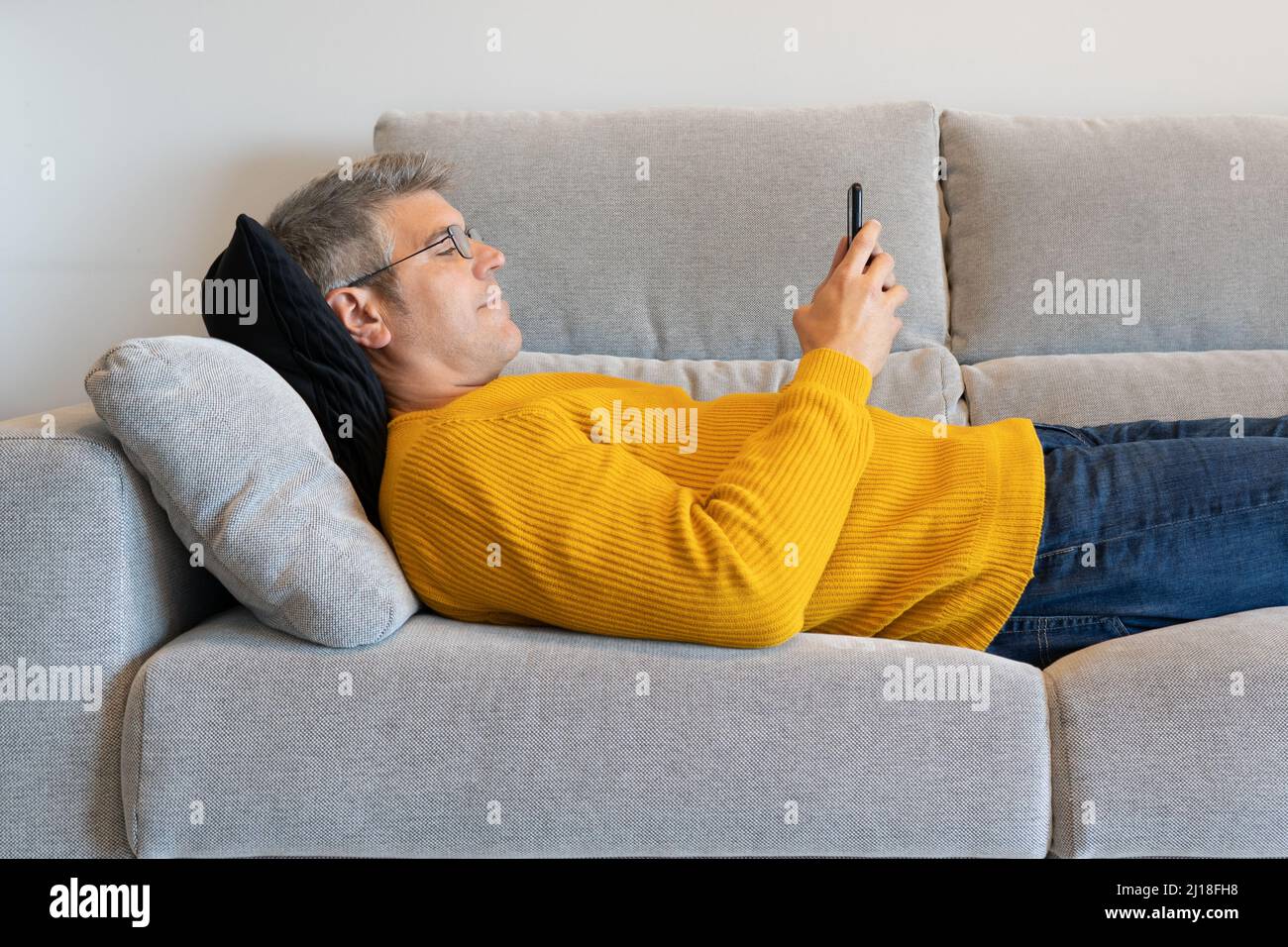 Homme avec des lunettes couché sur le canapé en tapant sur le téléphone portable. À la maison Banque D'Images