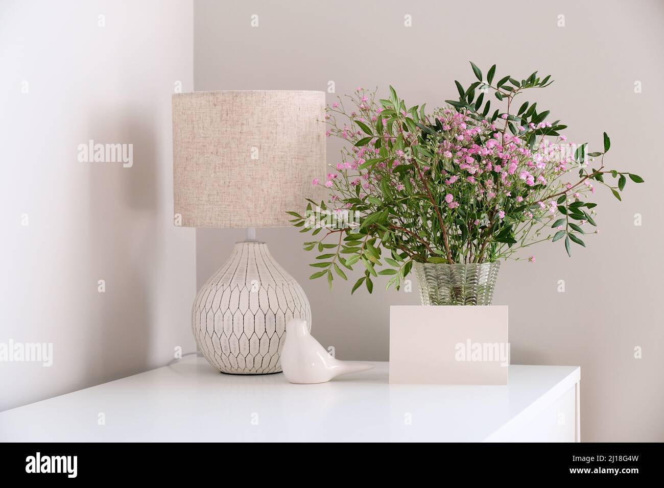 Table de bureau confortable avec lampe, bouquet de fleurs printanières dans un vase, maquette de carte de vœux. Hygge, style boho, salon scandinave Banque D'Images