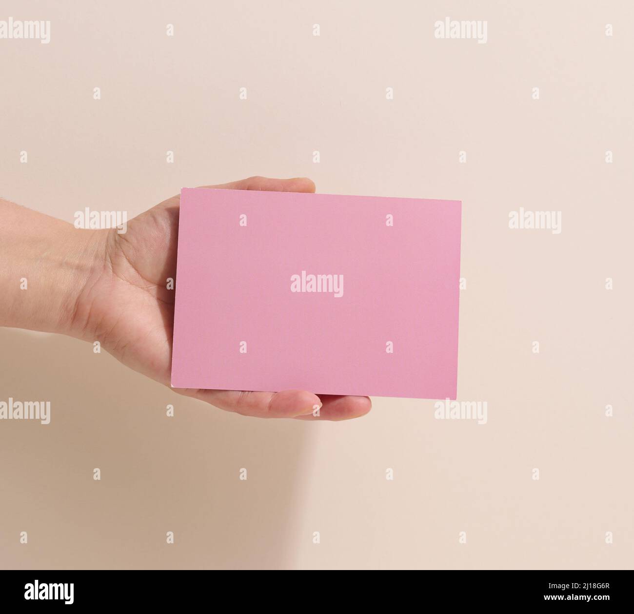 Main féminine tenant du papier rose vide sur fond beige.Copier/coller l'image ou le texte, gros plan Banque D'Images