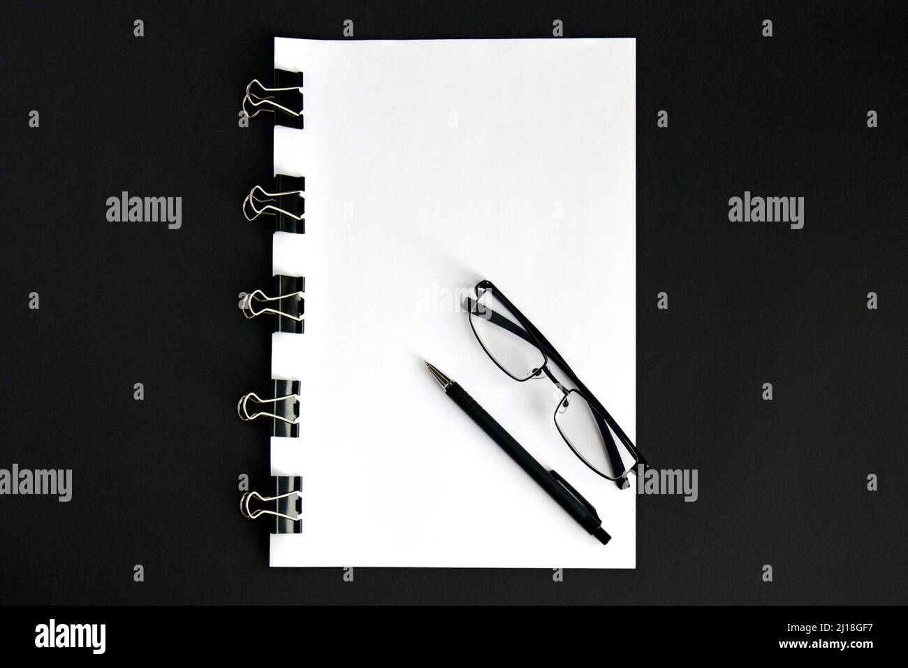 Feuilles blanches, stylo, lunettes et dispositif de reliure pour lier les feuilles de papier ensemble sur fond noir gros plan Banque D'Images