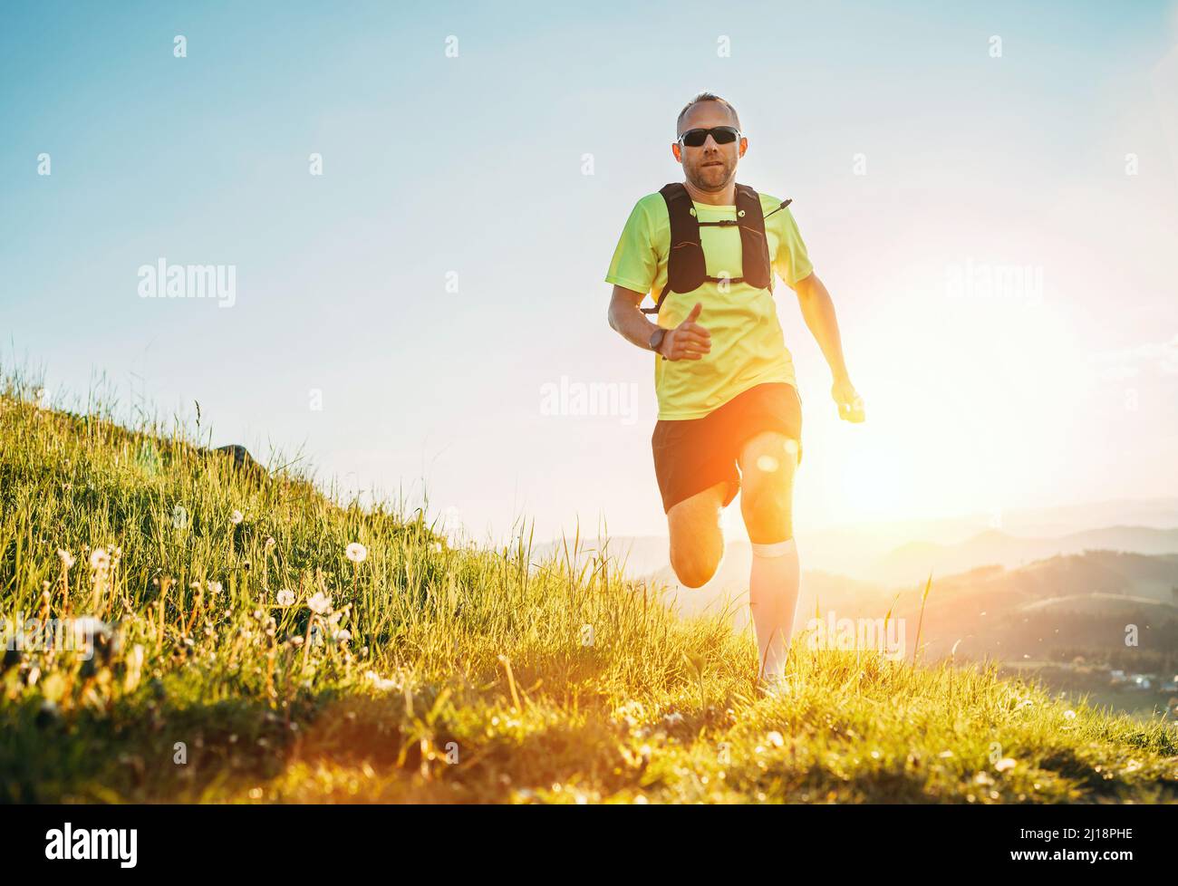 Active montagne Trail coureur habillé t-shirt brillant avec sac à dos dans sport lunettes de soleil course d'endurance marathon par les collines pittoresques au coucher du soleil t Banque D'Images