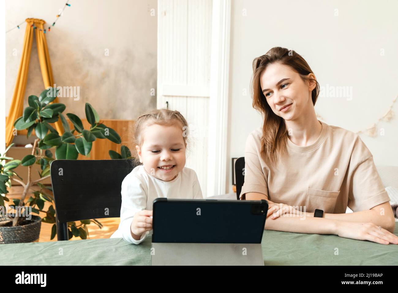 Formation à distance. Maman avec sa petite fille en train d'apprendre en ligne à la maison pendant la pandémie de Covid-19. Maman et petit bébé se rasent avec joie Banque D'Images