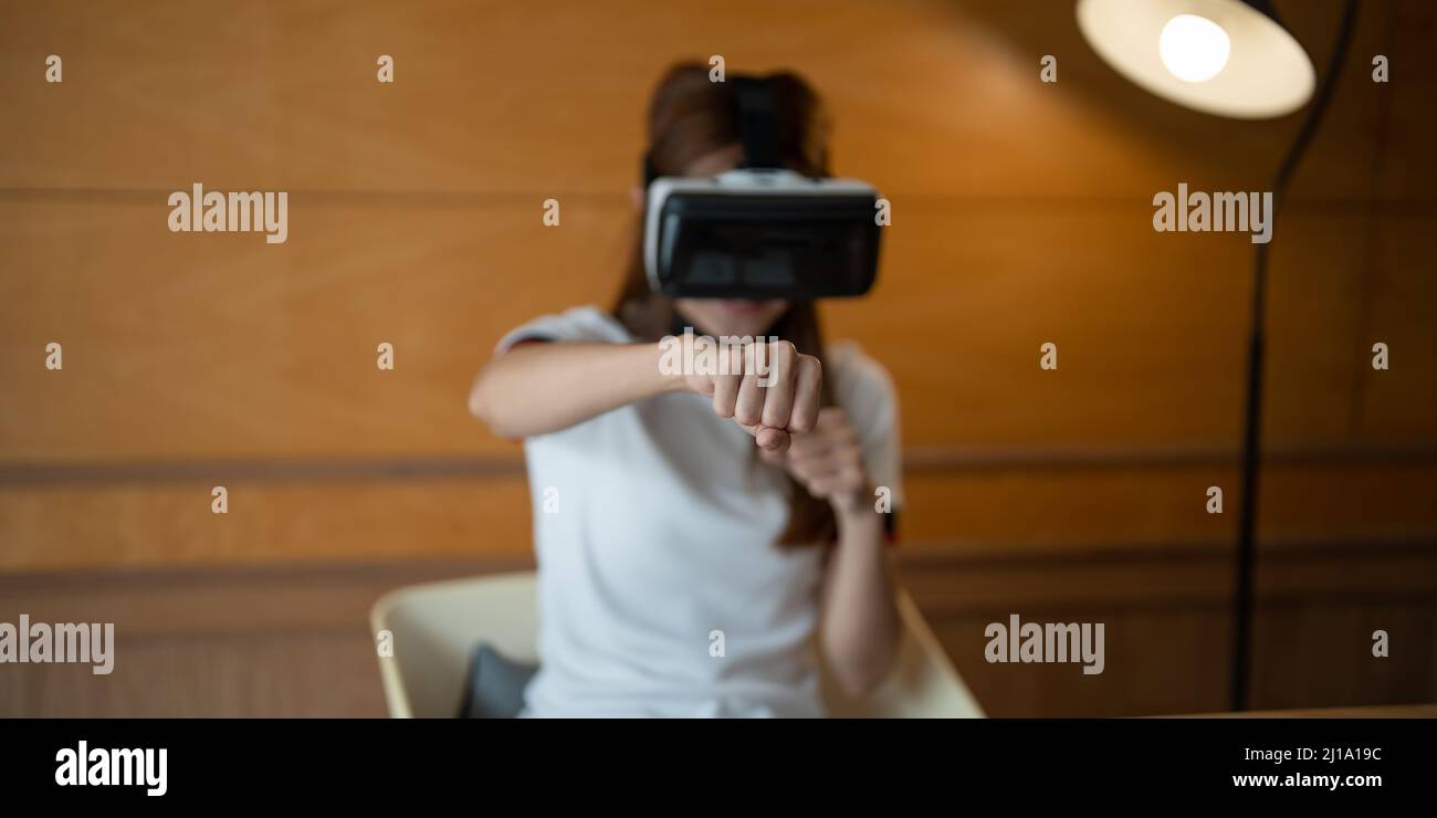 Fille portant des lunettes de réalité virtuelle à la tête jouant au jeu de combat, tenant les poings serrés prêts à la boxe, en faisant l'expérience du cyberespace à l'aide de la VR Banque D'Images