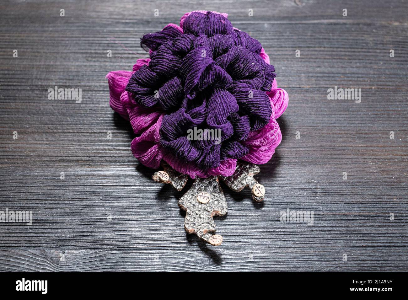 broche en cuir et soie artisanale stylisée comme une fleur de chrysanthème sur un panneau en bois sombre Banque D'Images