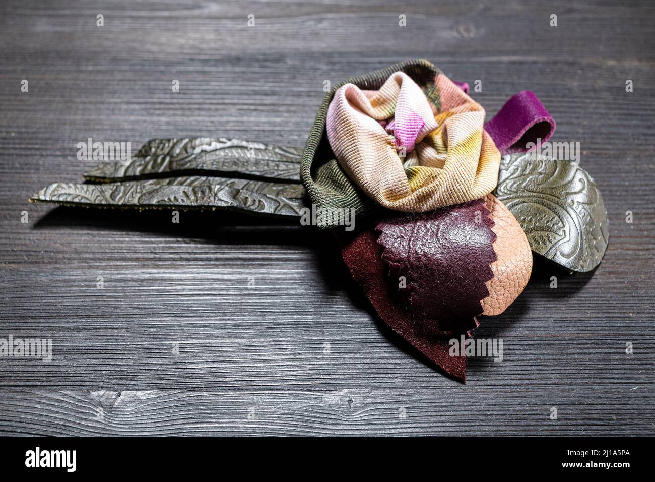 broche en cuir et soie artisanale stylisée comme une fleur rose sur un panneau en bois sombre Banque D'Images