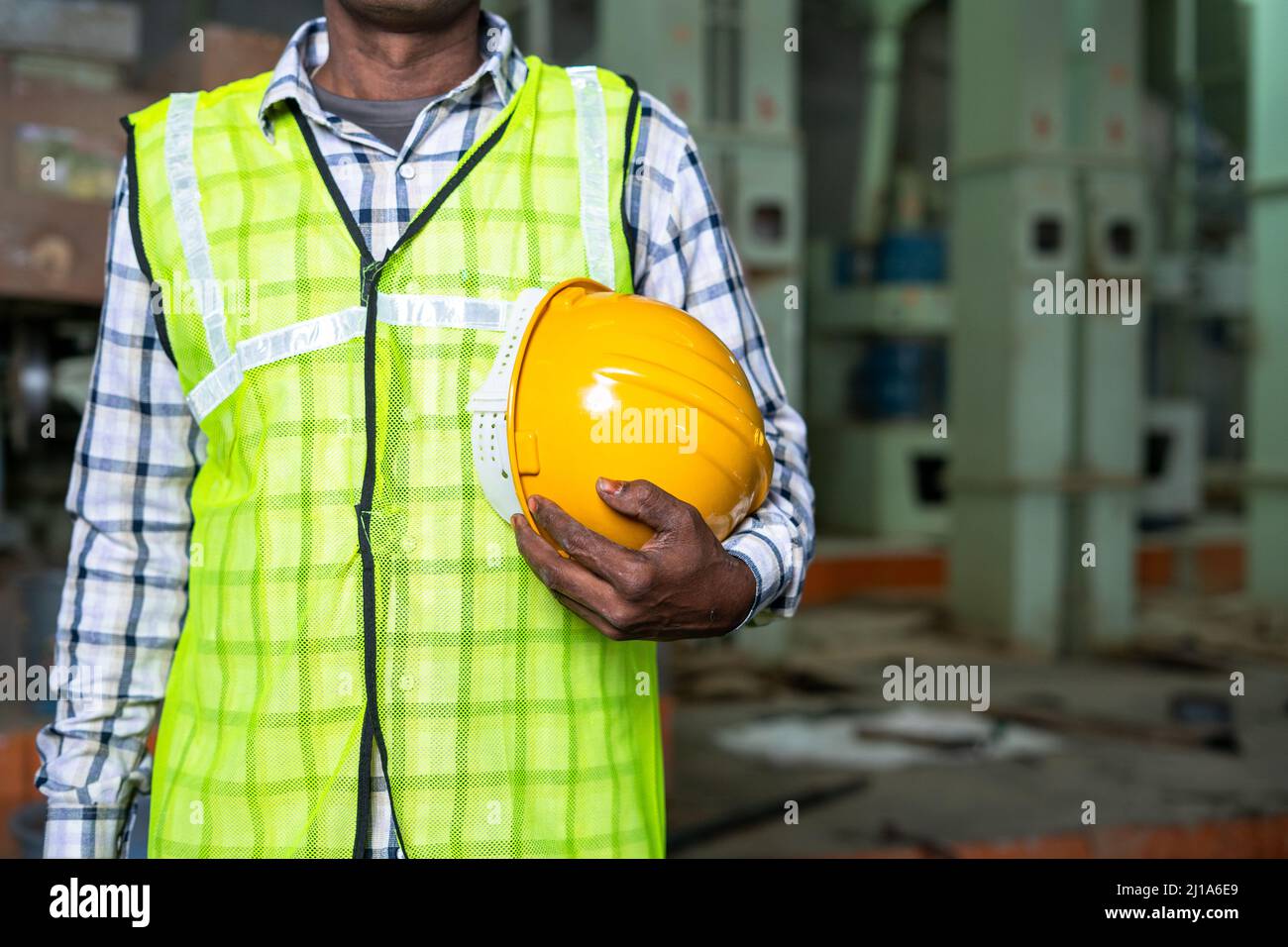Gros plan d'un travailleur de l'industrie debout en tenant un casque de sécurité en usine - concept de matériel de travail, mesures de sécurité et travail à col bleu. Banque D'Images