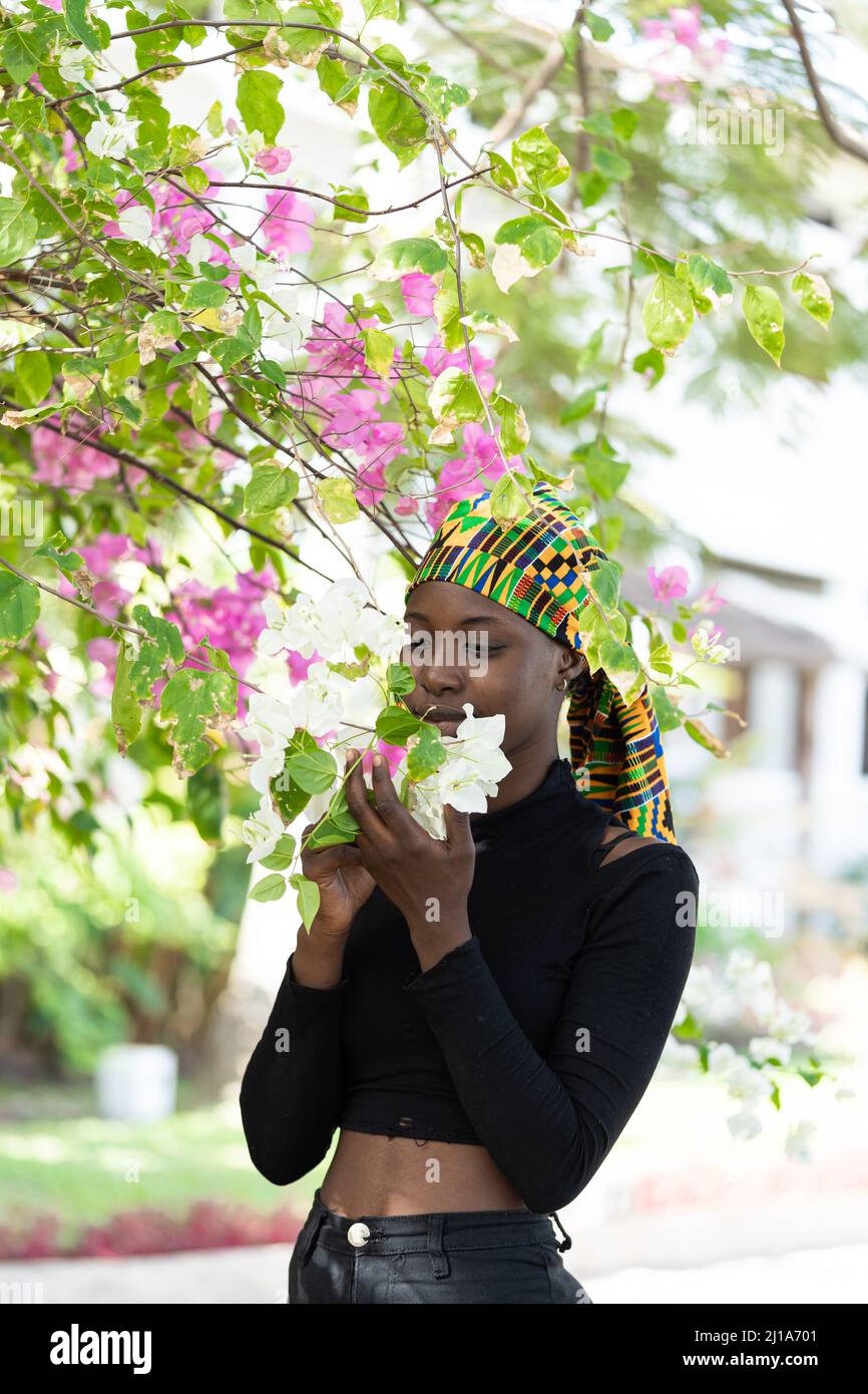 Charmante jeune femme africaine caressant doucement les délicates fleurs d'une plante de bougainvilliers, symbole de romance, d'harmonie et de tendresse Banque D'Images