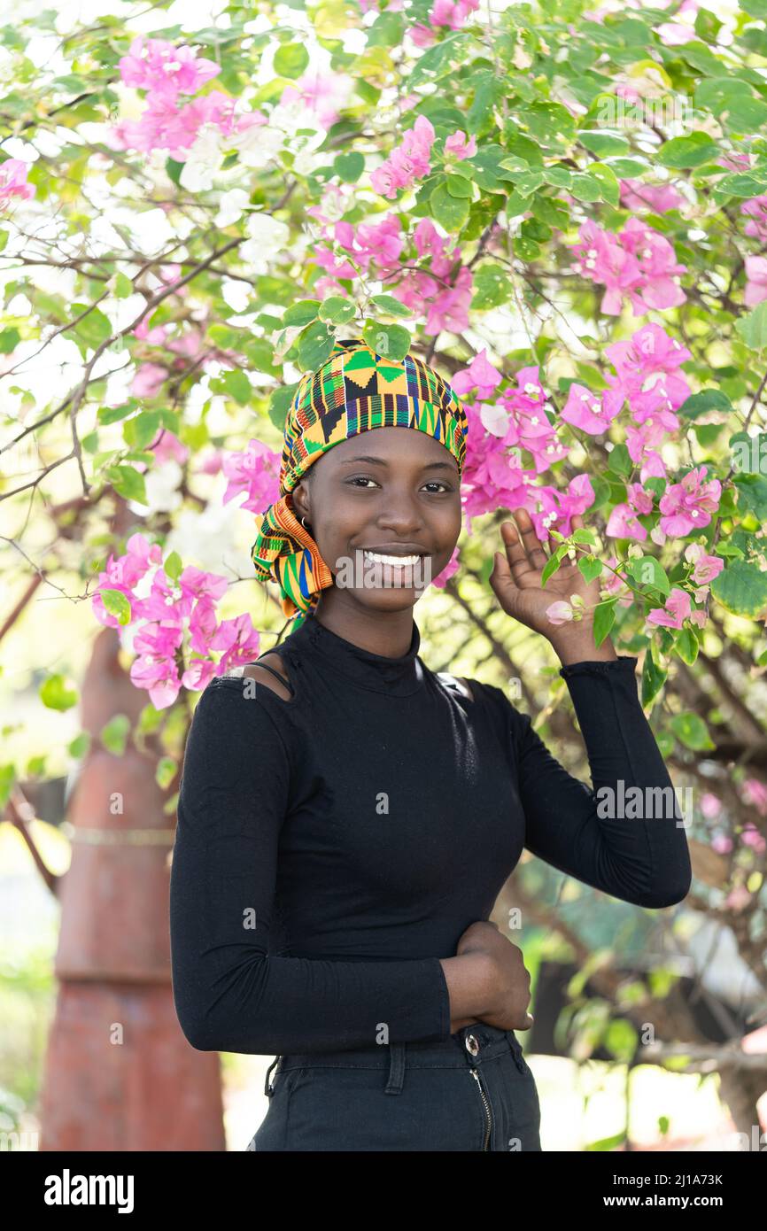 Magnifique fille africaine sous une arche naturelle de fleurs roses et blanches luxuriantes, un symbole de la jeunesse bourgeonnante, de la santé et de l'énergie Banque D'Images