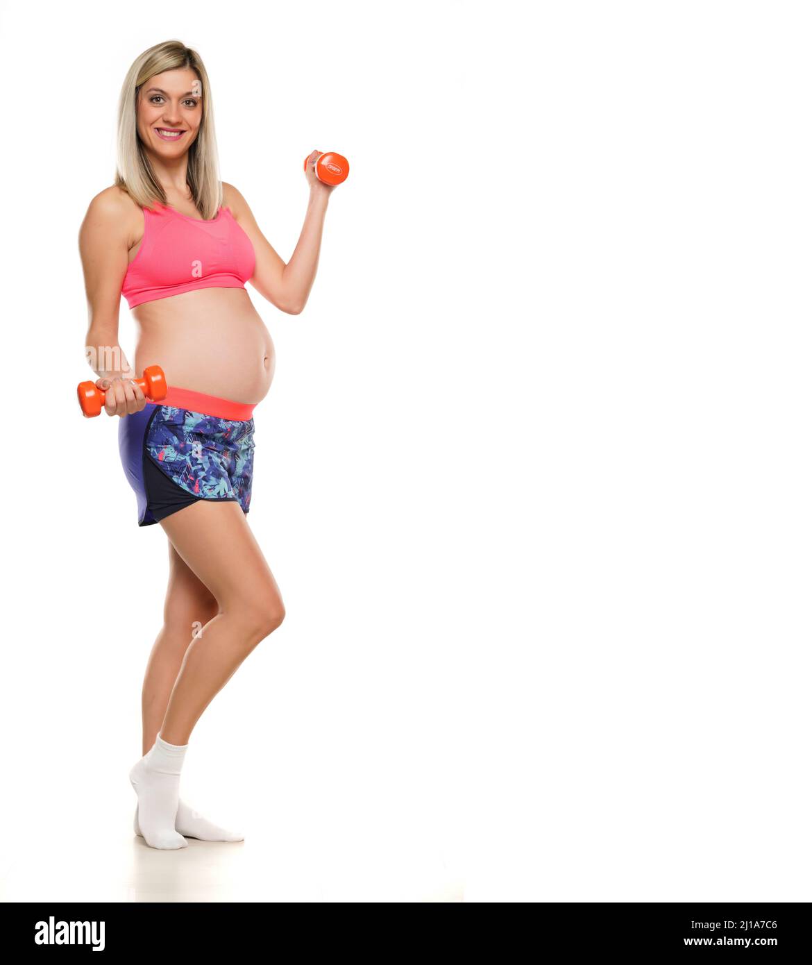 Femme enceinte souriante levant des poids sur un fond blanc Banque D'Images