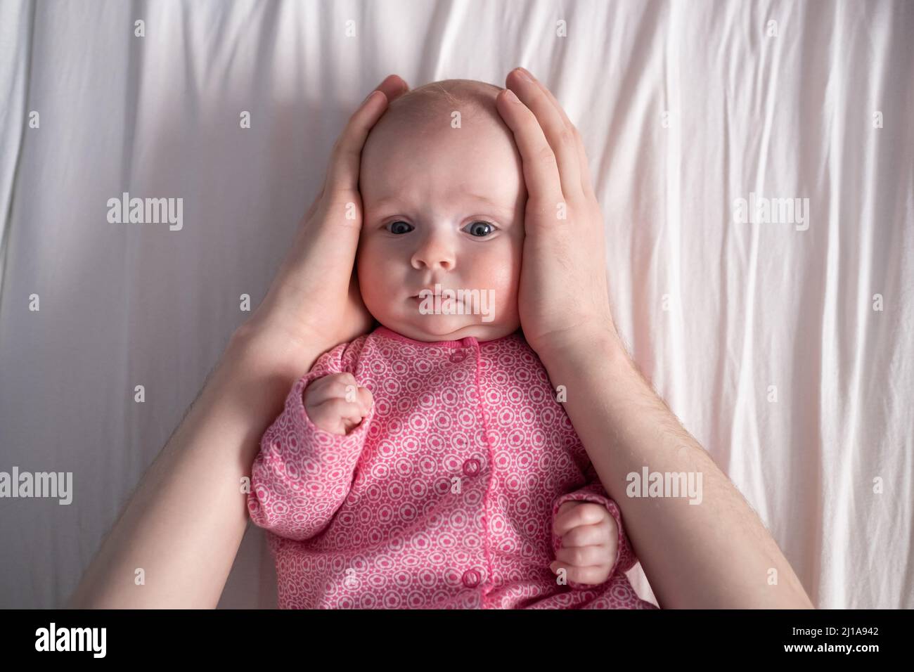 Petite fille couchée, la main de la mère appuyant ses joues et la tête. Banque D'Images