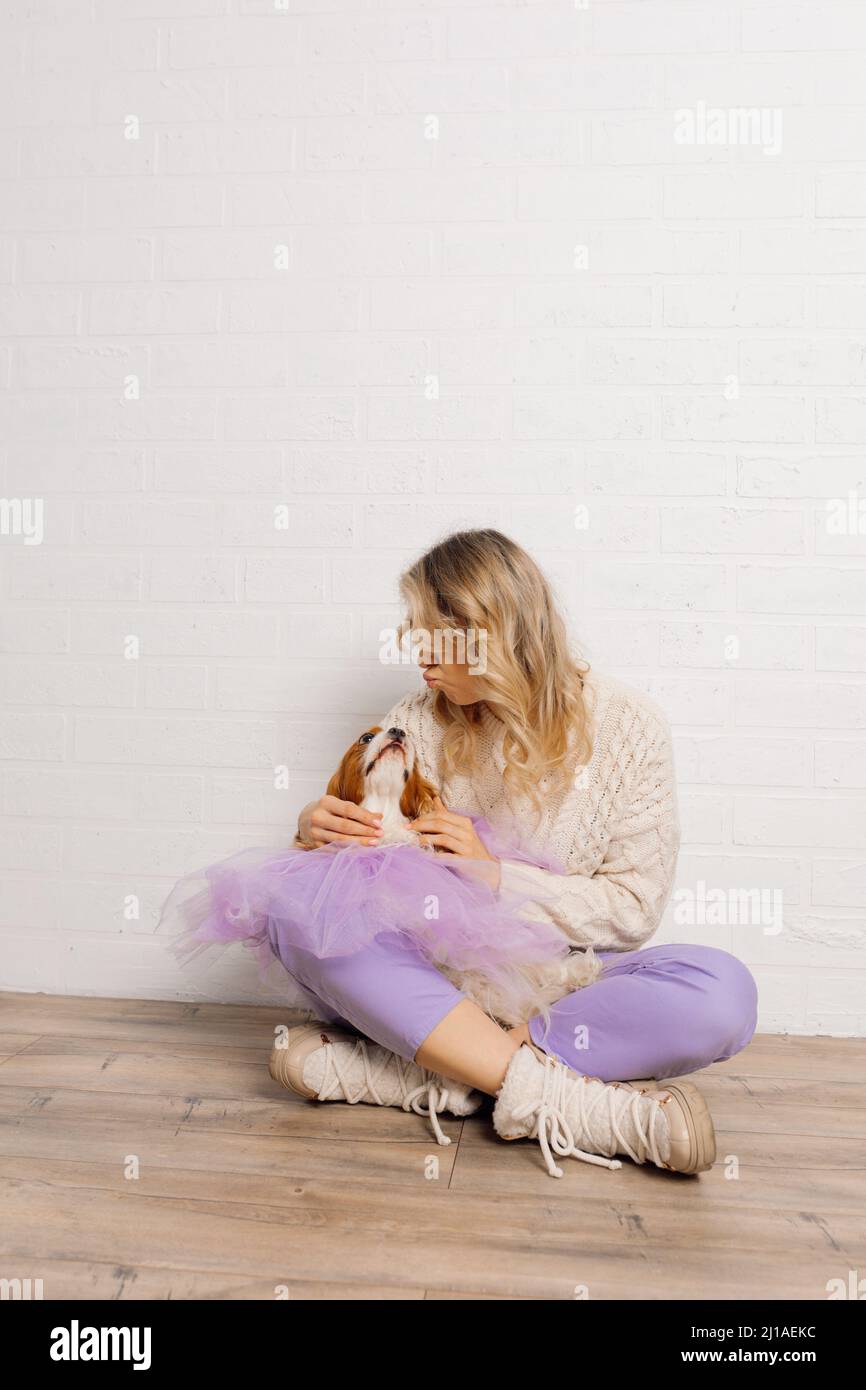 Une femme bien entretenue, tenue en chandail beige et pantalon violet, envoie des baisers au chien de spaniel dans le cape organza violet Banque D'Images