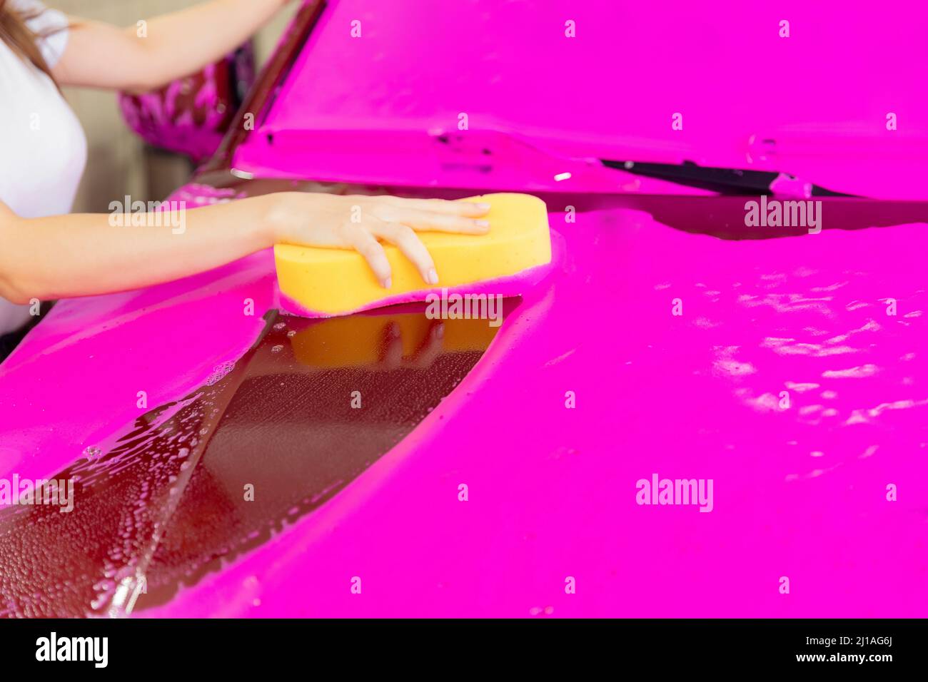 Tenir à la main l'éponge jaune sur la voiture pour laver le fond en mousse rose. Banque D'Images