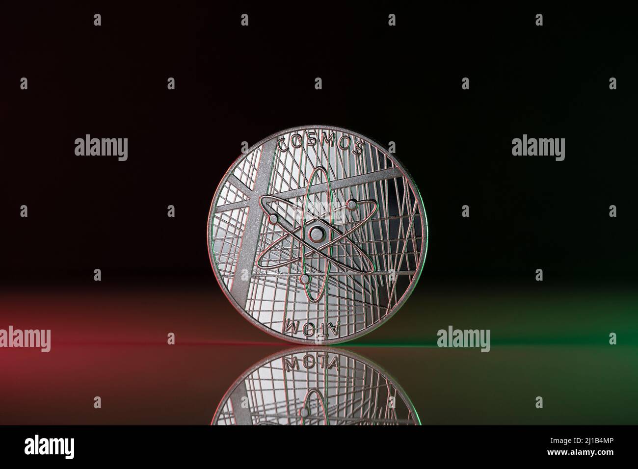 La pièce de monnaie physique de crypto-monnaie COSMOS ATOM est placée sur une surface réfléchissante et éclairée par les lumières verte et rouge. Banque D'Images