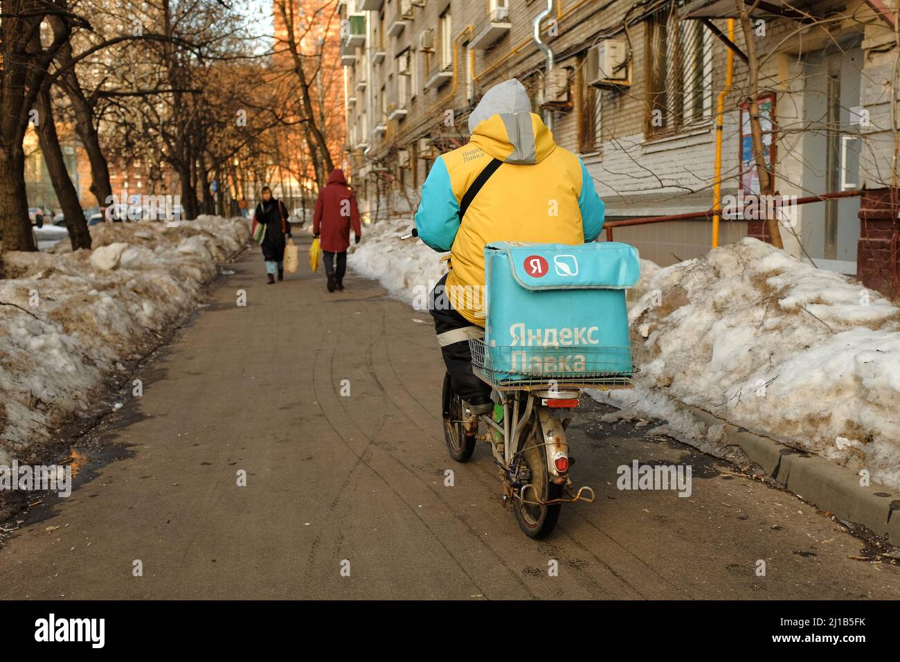 Moscou, Russie - 25 février 2022 : un messager de Yandex lavka sur un mobylette fait maison livre des provisions et des promenades sur le trottoir en hiver Banque D'Images