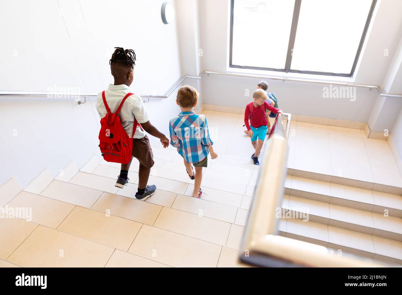 Vue en grand angle des écoliers multiraciaux avec sacs à dos sur les marches dans le bâtiment de l'école Banque D'Images