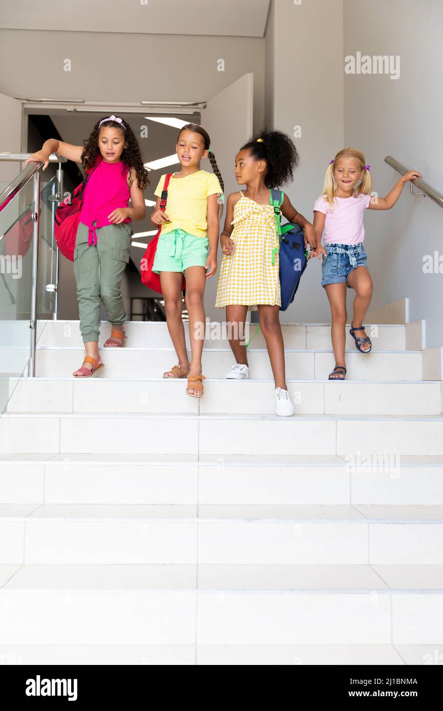 Filles d'école primaire multiraciale avec des sacs à dos sur les marches dans le bâtiment de l'école Banque D'Images