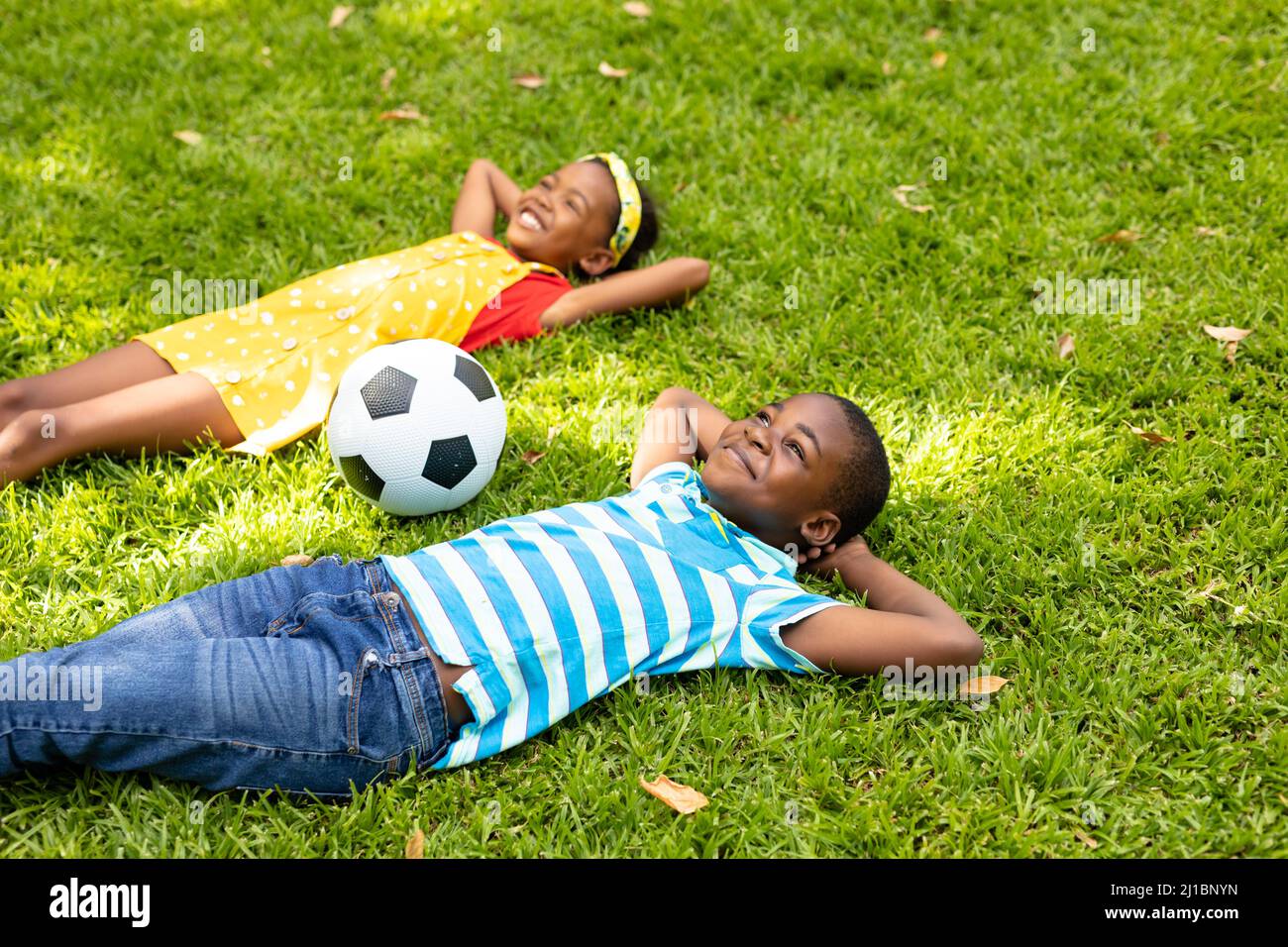 Un garçon et une fille afro-américains souriants, allongé avec les mains derrière la tête par un ballon de football dans l'arrière-cour Banque D'Images