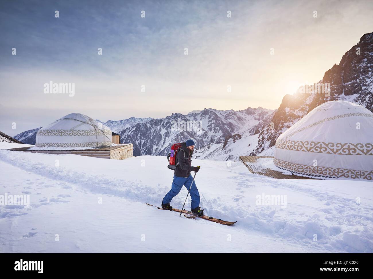 Skieur homme ski en montant avec la barbe et le sac à dos à haute montagne enneigée près de la maison de yourte traditionnelle nomade à la station de ski de Shymbulak à Almaty, Kazak Banque D'Images