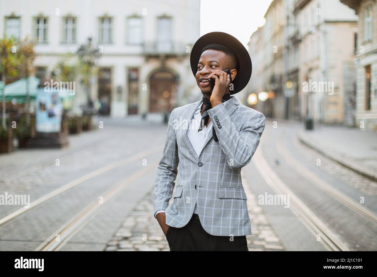 Homme afro-américain élégant en chapeau noir ayant la conversation mobile  tout en se tenant dans la rue de la ville. Jeunes hommes hipster marche et  en plein air Photo Stock - Alamy