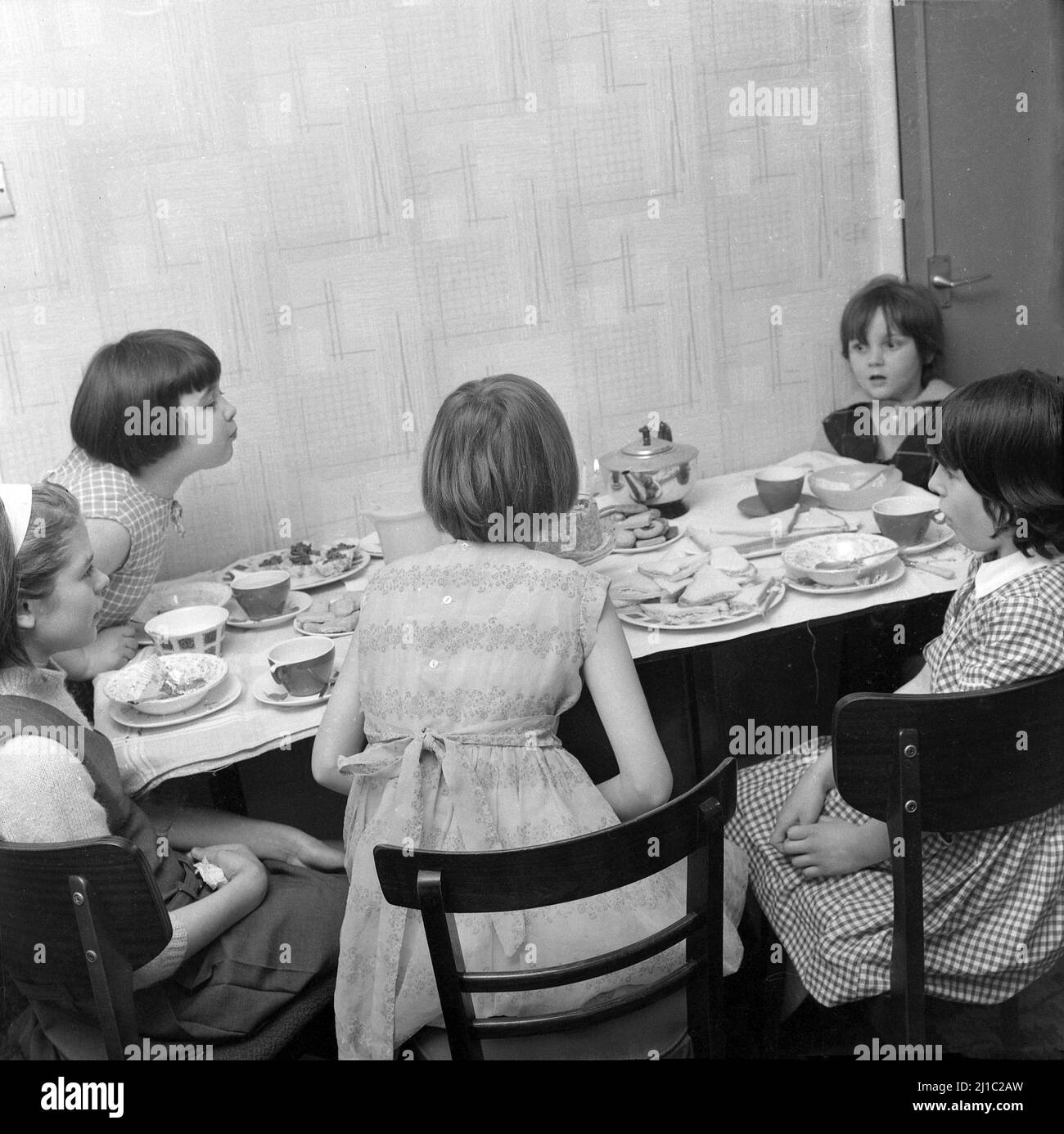 1960s, historique, fête de thé d'anniversaire, cinq jeunes filles s'asseyaient autour d'une table de cuisine, l'une d'entre elles se penchait pour souffler les bougies sur le gâteau, Manchester, Angleterre, Royaume-Uni. Banque D'Images