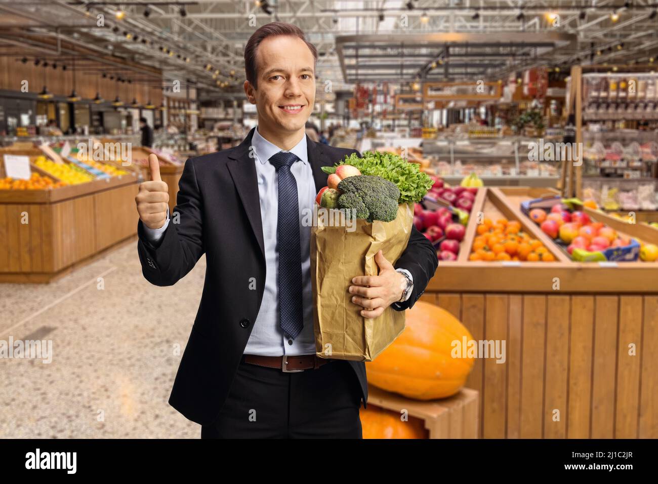 Bussinesman tenant un sac en papier avec des produits d'épicerie et montrant les pouces vers le haut à l'intérieur d'un magasin Banque D'Images