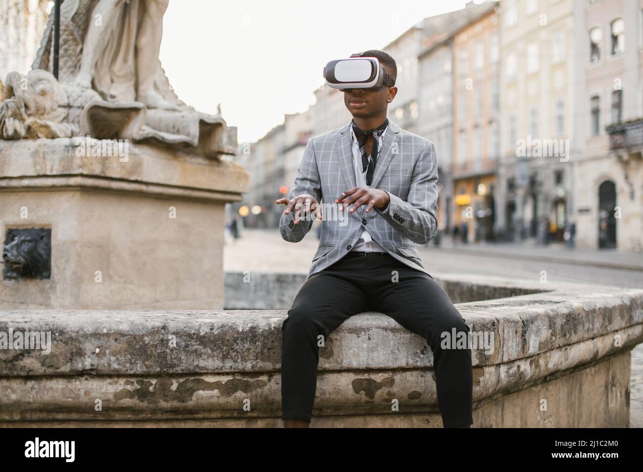 Homme afro-américain en costume d'affaires élégant assis dans la rue de la ville et à l'aide de lunettes VR. Concept de personnes, innovation et modes de vie modernes. Banque D'Images
