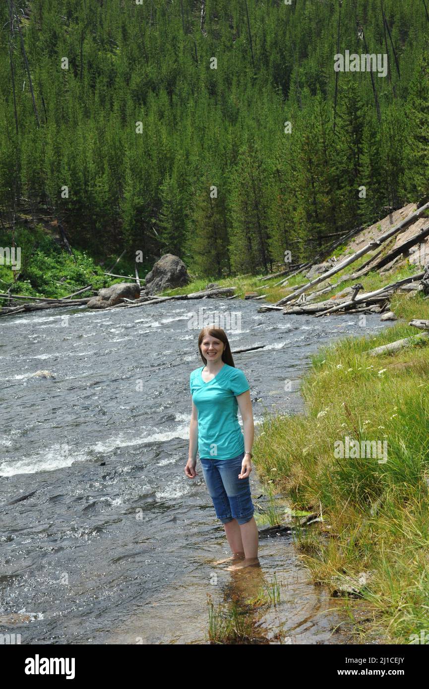 Une jeune femme attirante se jette dans la rivière Gibbon dans le parc national de Yellowstone. Son Jean est enroulé et il est à la cheville. Banque D'Images