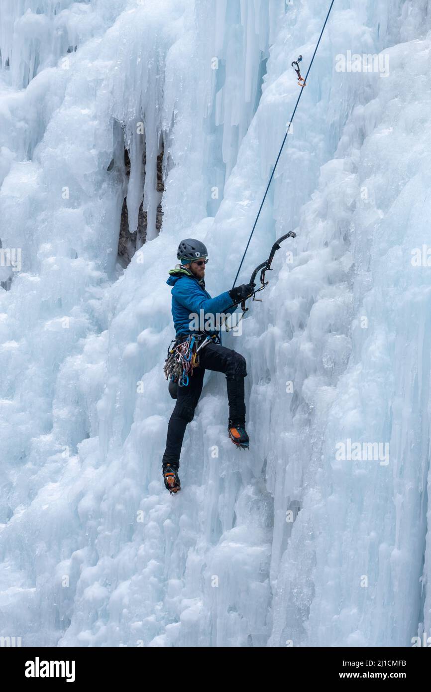 Un grimpeur de glace enlève un point d'ancrage de vis de glace alors qu'il monte un mur de glace de 160 pi de haut dans le parc de glace d'Ouray, Colorado, Banque D'Images