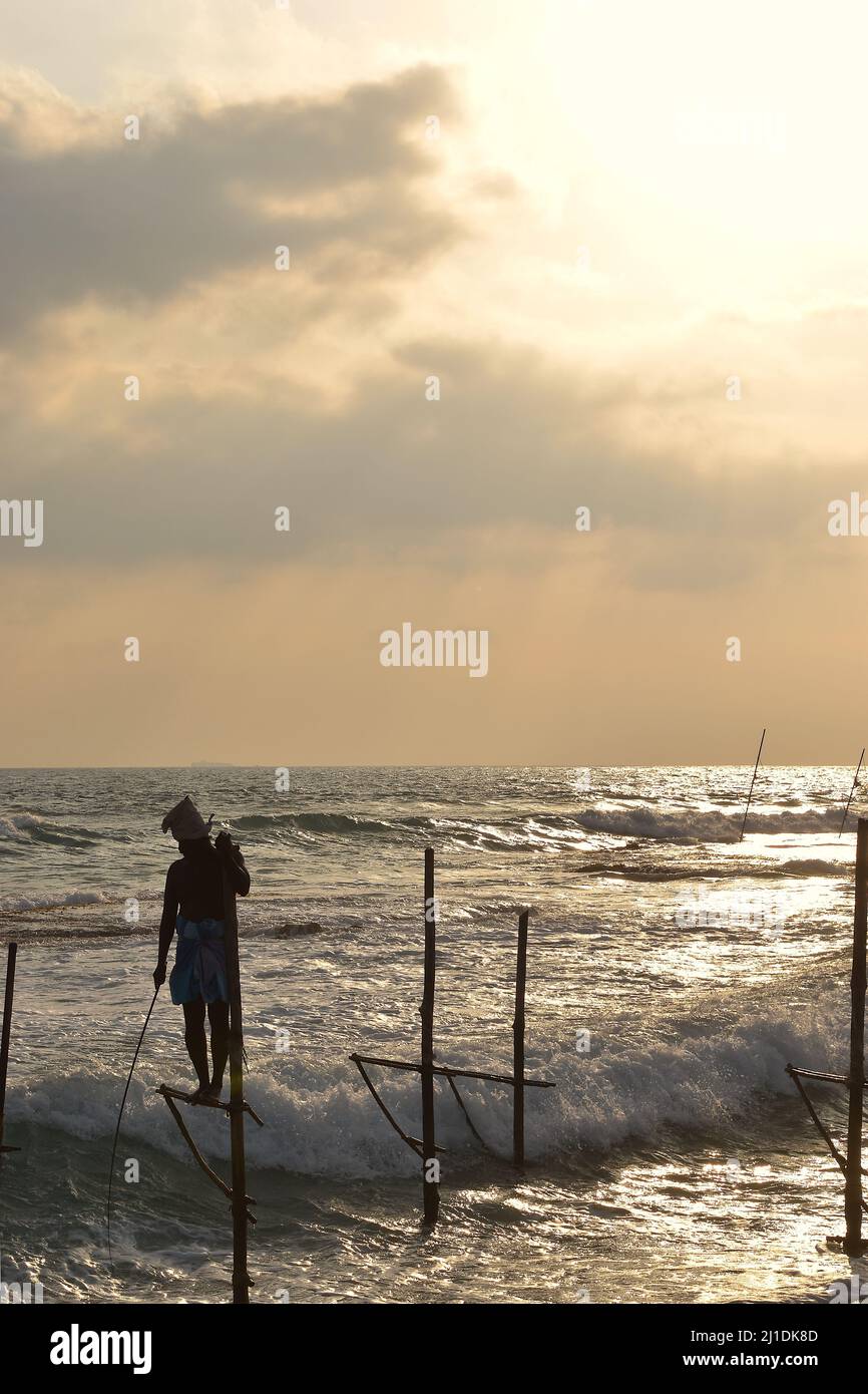 Silhouette de pêcheur sur pilotis au coucher du soleil, sur la côte sud du Sri Lanka Banque D'Images