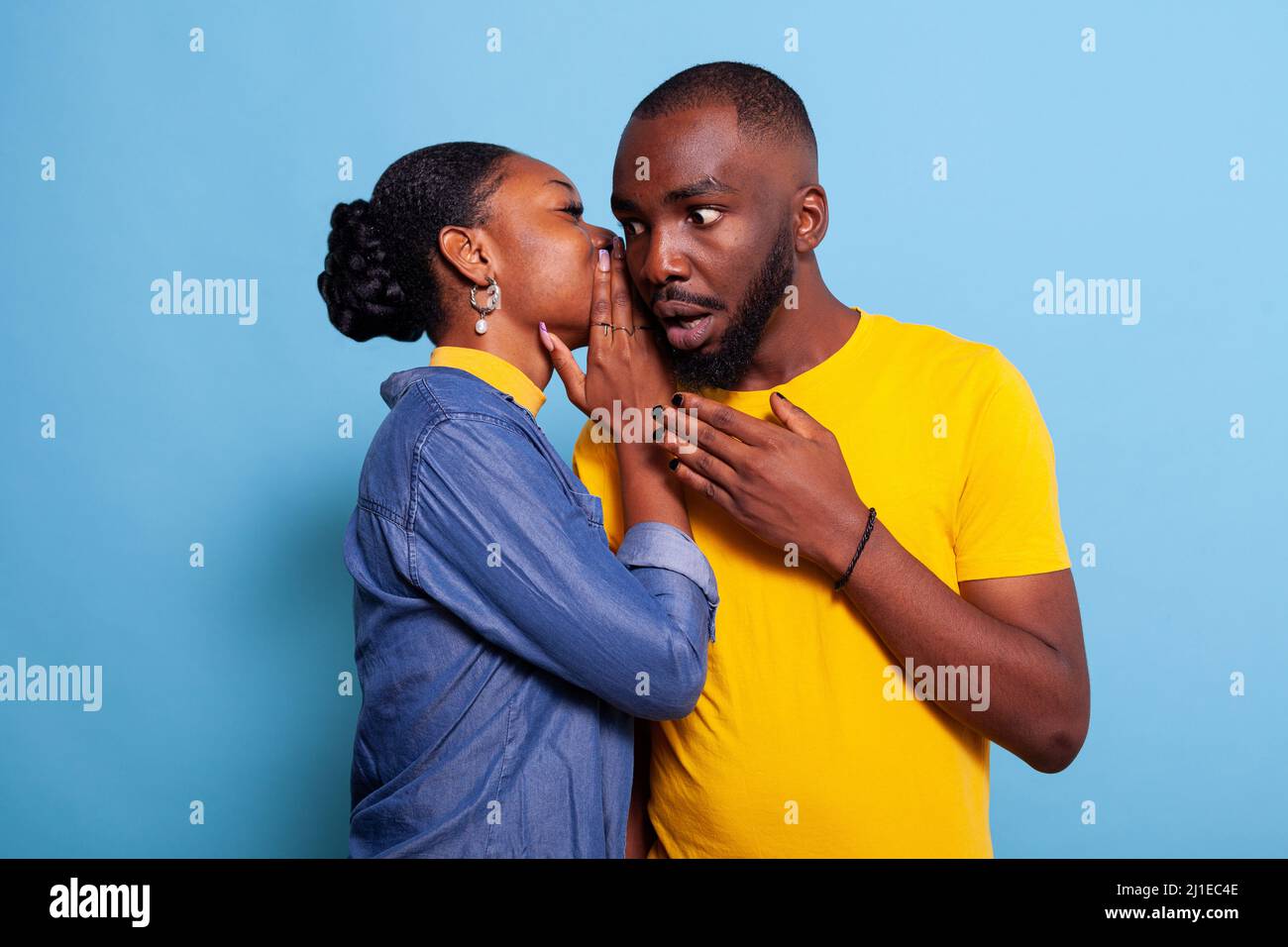 Homme surpris de découvrir des potins secrets de la petite amie en studio. Une jeune femme chuchote le rumeur à l'oreille d'un petit ami, ayant une conversation confidentielle. Personne curieuse à l'écoute de la maltraitance. Banque D'Images