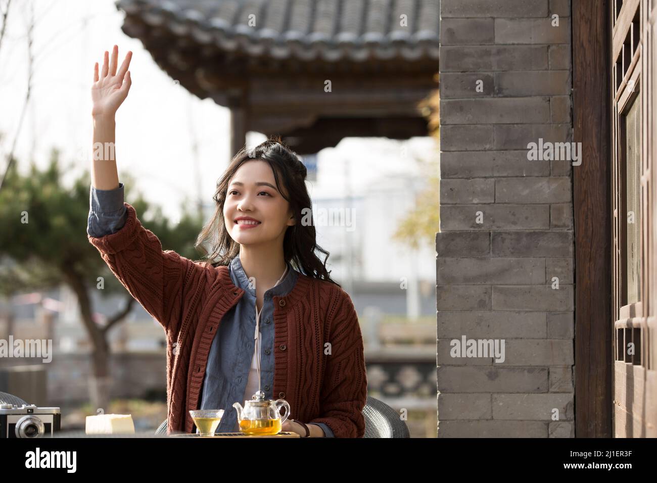 Une femme chinoise saluant un ami et prenant le thé de l'après-midi dans un café-terrasse - photo de stock Banque D'Images