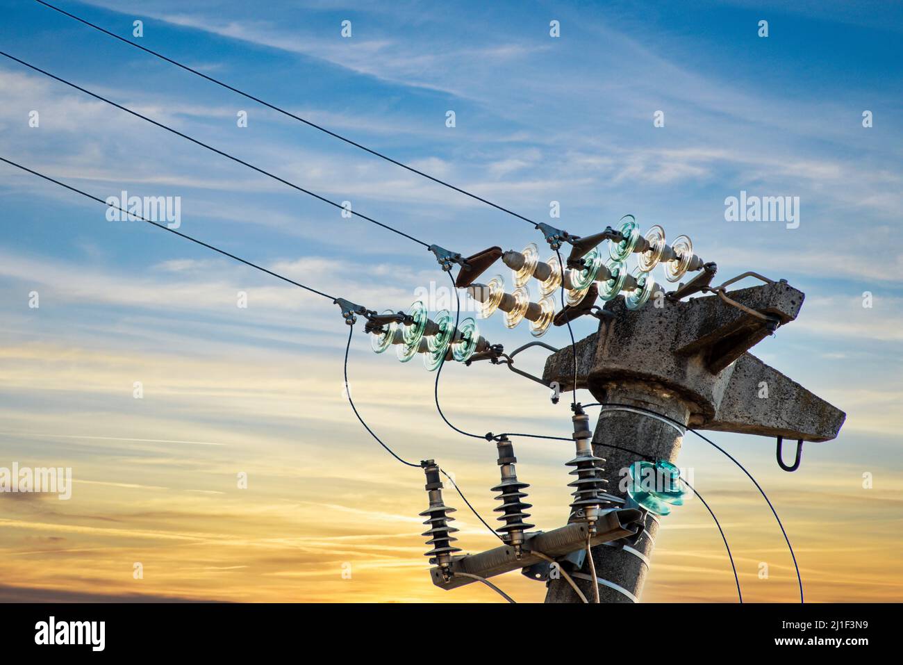 Poteau électrique en béton avec isolants en verre sur les câbles électriques, sur ciel jaune et bleu au coucher du soleil Banque D'Images