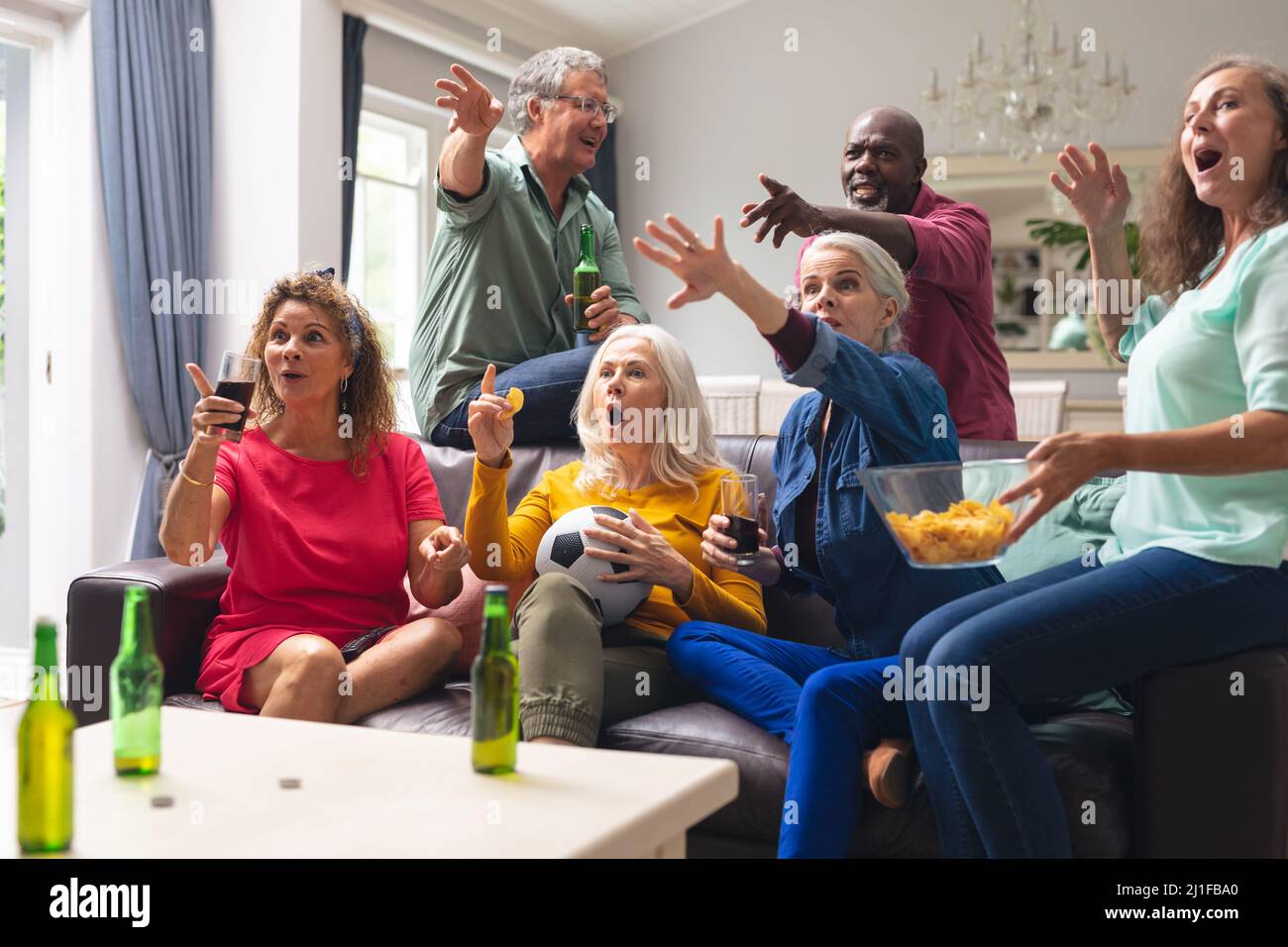 Des amis séniors multiraciaux choqués regardant un match de football à la télévision à la maison Banque D'Images