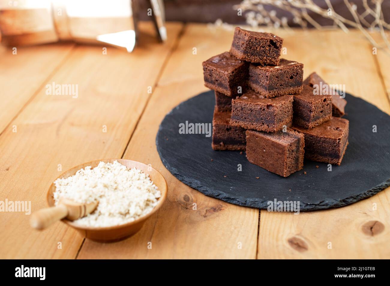 Carrés Brownie empilés sur une tuile de pierre noire à côté d'un bol rempli de noix hachées Banque D'Images