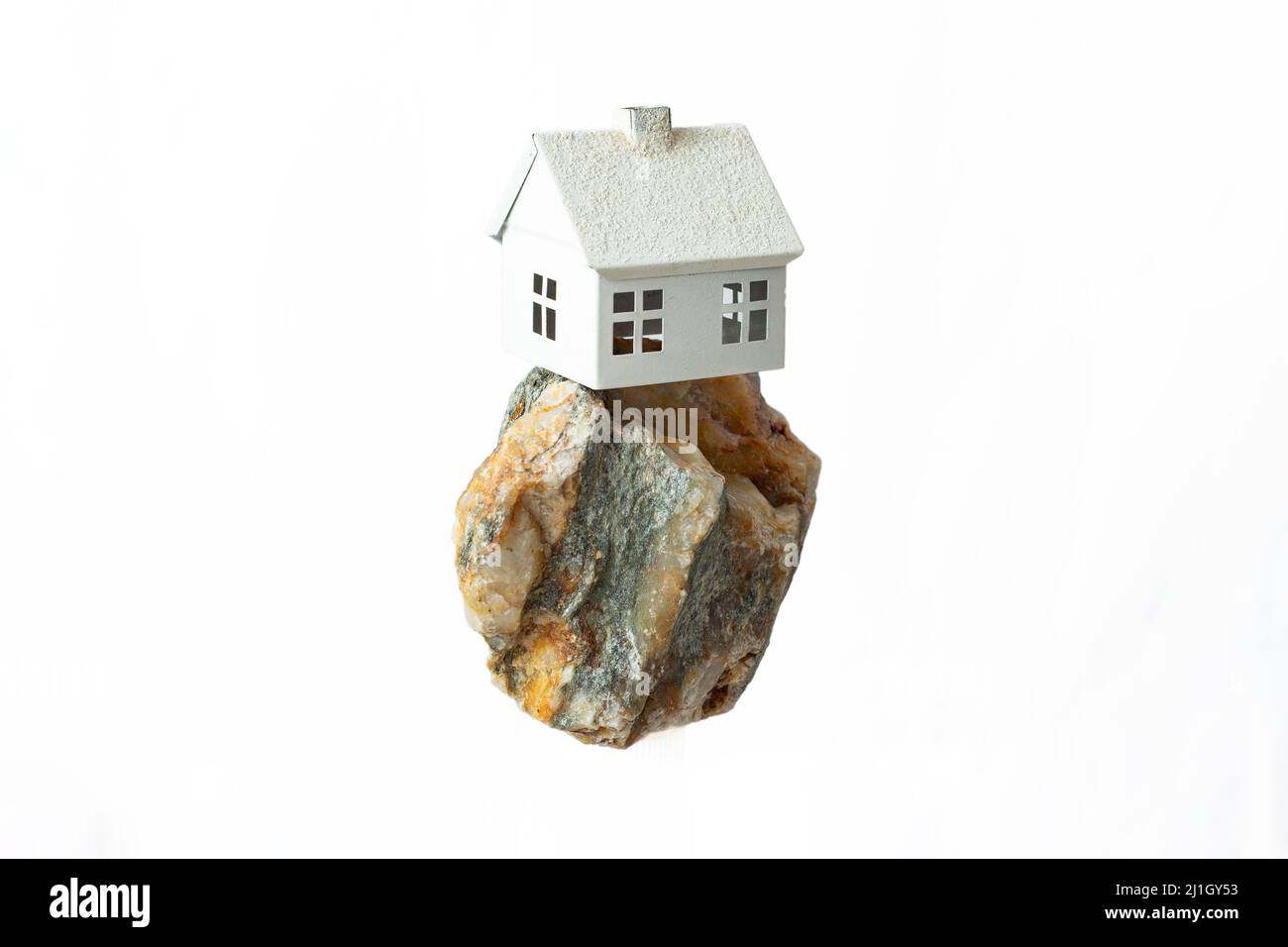 miniature maison modèle levant sur un grand rocher, isolé sur fond blanc Banque D'Images