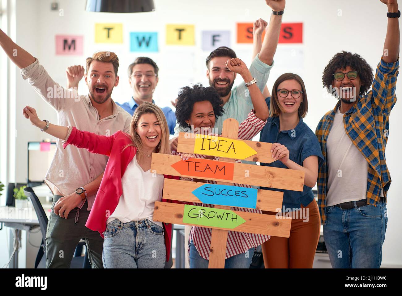 Un groupe de travailleurs de bureau heureux posent pour une photo tout en tenant un panneau avec des slogans de compagnie dans une atmosphère agréable dans le bureau. Employés, JO Banque D'Images