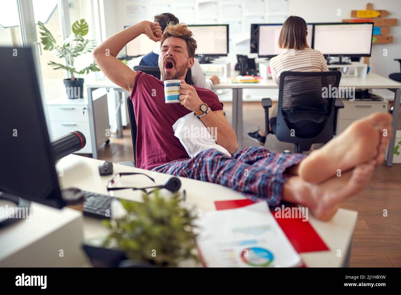 Un jeune employé de sexe masculin tente de rester éveillé tout en travaillant dans une atmosphère monotone au bureau. Employés, travail, bureau Banque D'Images
