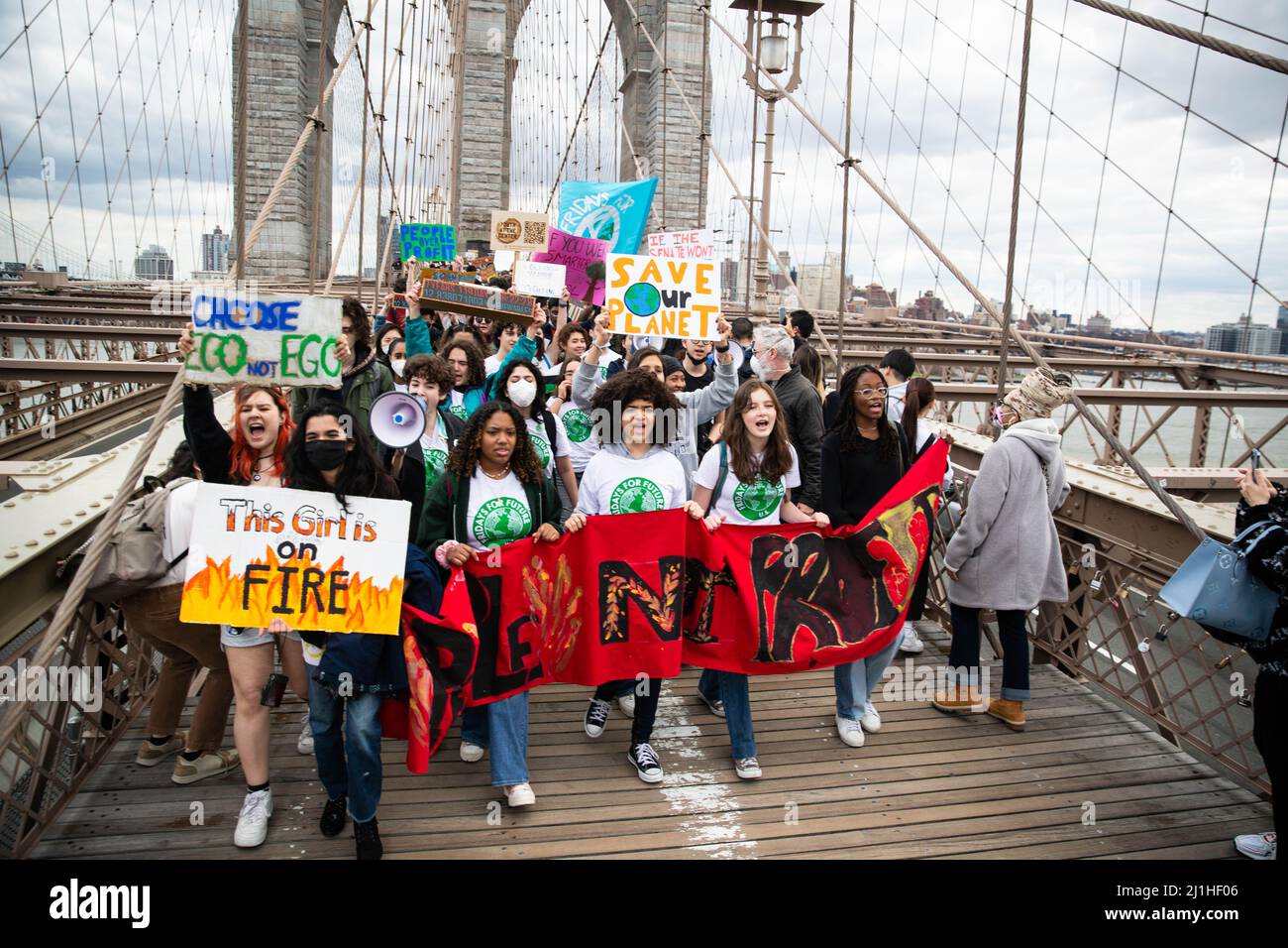 New York, États-Unis. 25th mars 2022. Les jeunes manifestants pour le climat scandent des slogans et tiennent une bannière lorsqu'ils traversent le pont de Brooklyn. Plus d'un millier de jeunes activistes du climat ont défilé de Brooklyn Borough Hall, de l'autre côté du pont de Brooklyn à Foley Square, dans le cadre d'une grève mondiale du climat. Crédit : SOPA Images Limited/Alamy Live News Banque D'Images