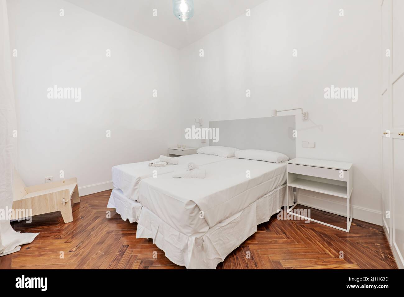 Chambre avec lits doubles et draps blancs, serviettes de bain sur les lits, tables de chevet blanches et parquet en pin Banque D'Images