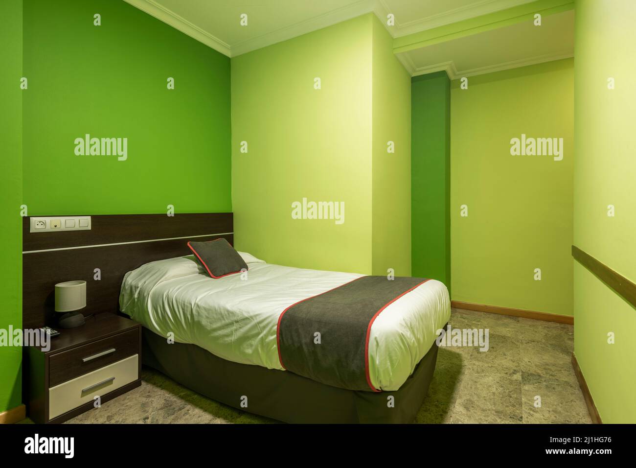 chambre avec petit lit en bois sombre avec table de nuit assortie, coussin et couverture marron avec garniture rouge et murs peints vert pistache Banque D'Images